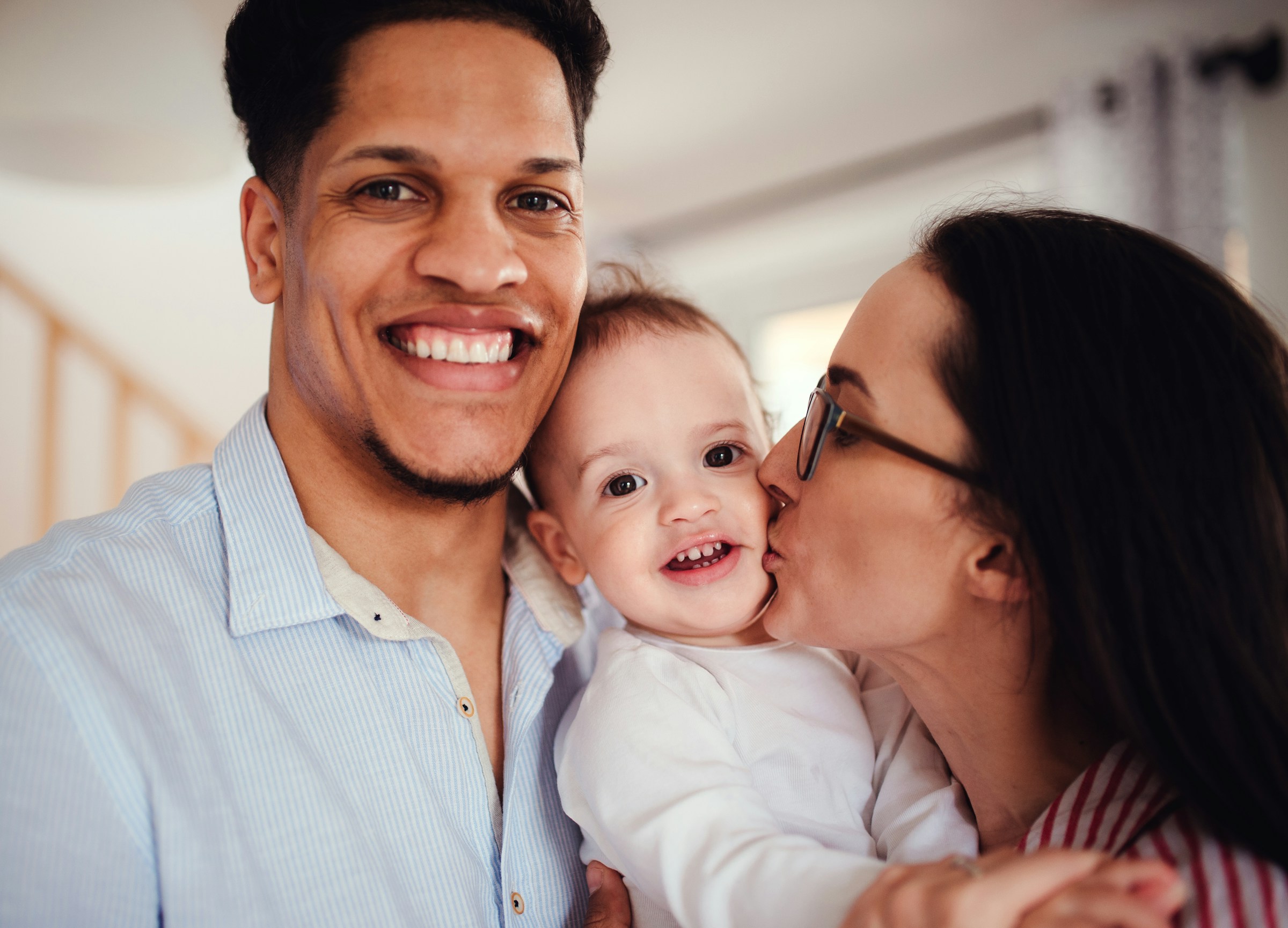 A smiling father and a mother kissing the baby in between them.