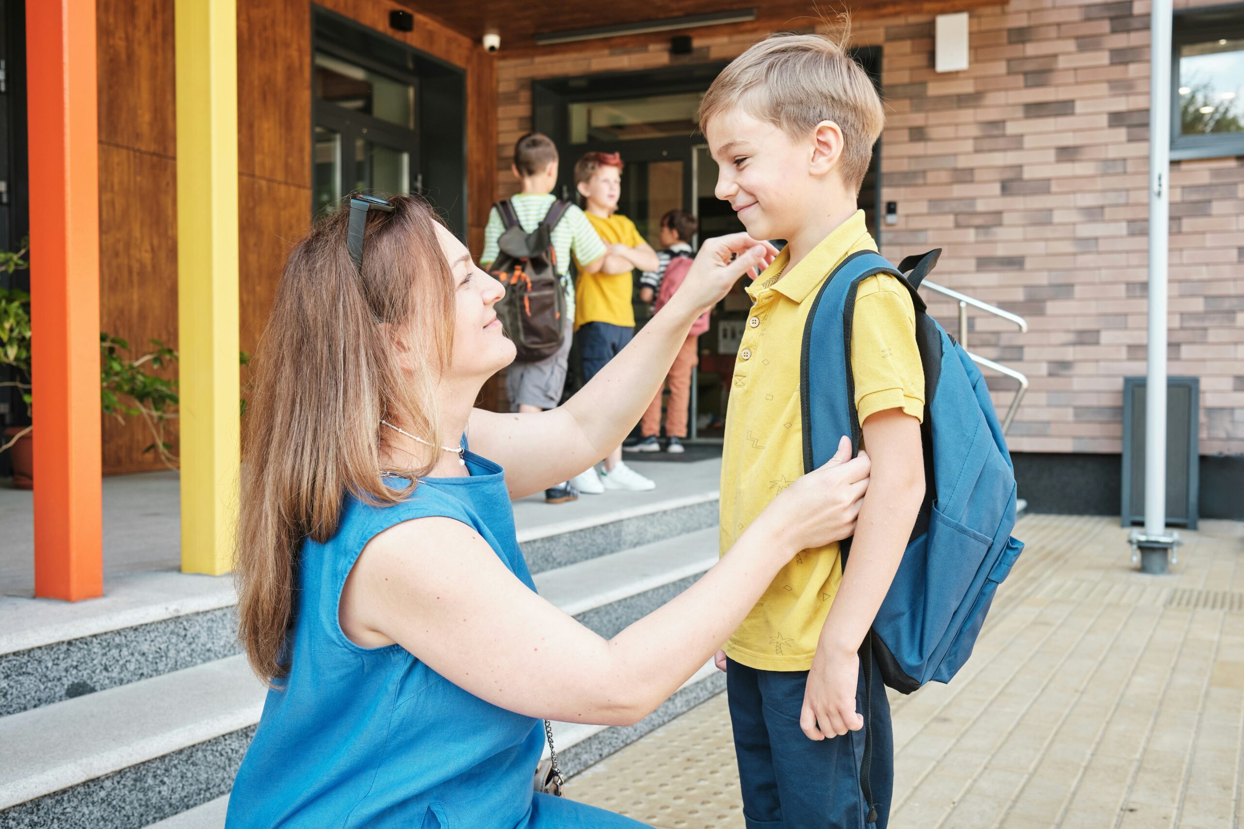 Mom kneeling in front of son before he walks into school