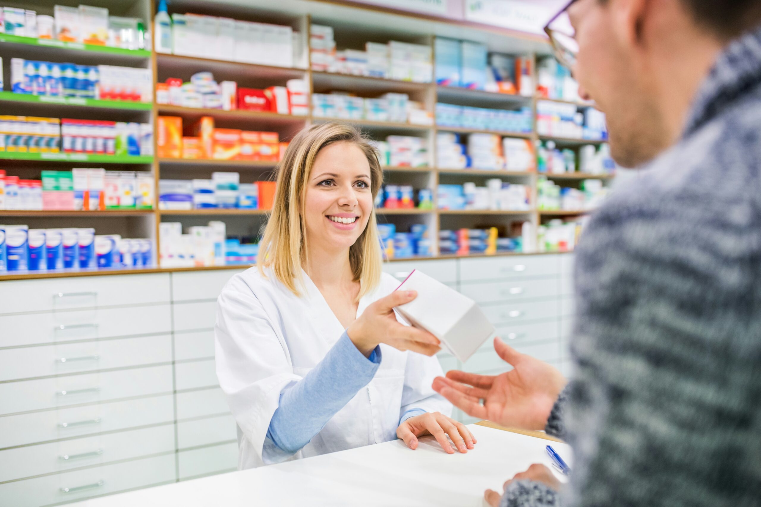 A young pharmacist smiles as she gives a patient a box of medicine