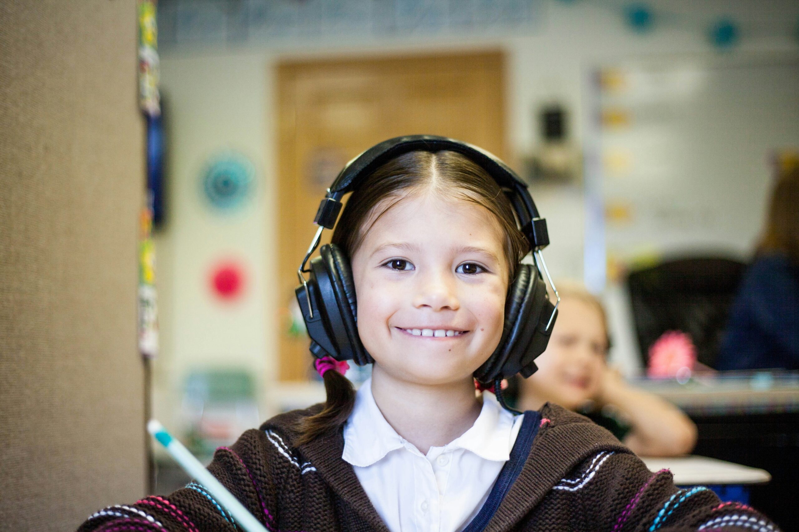 A young girl wearing headphones smiles in a classroom.