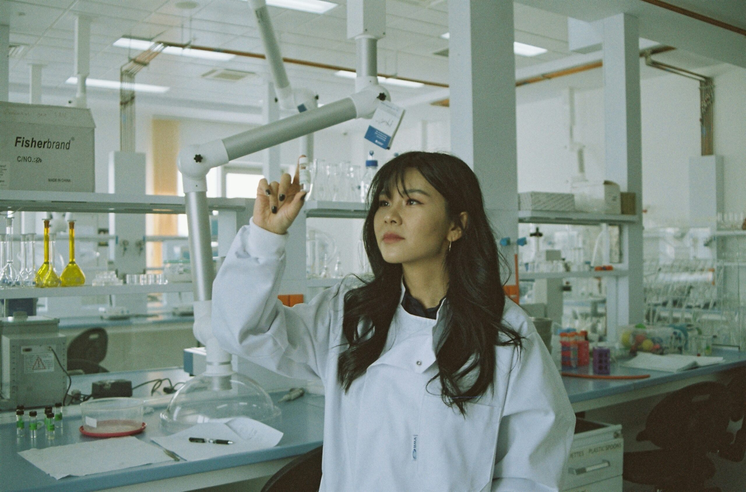 A young female researcher in a lab examines a specimen in a vial.