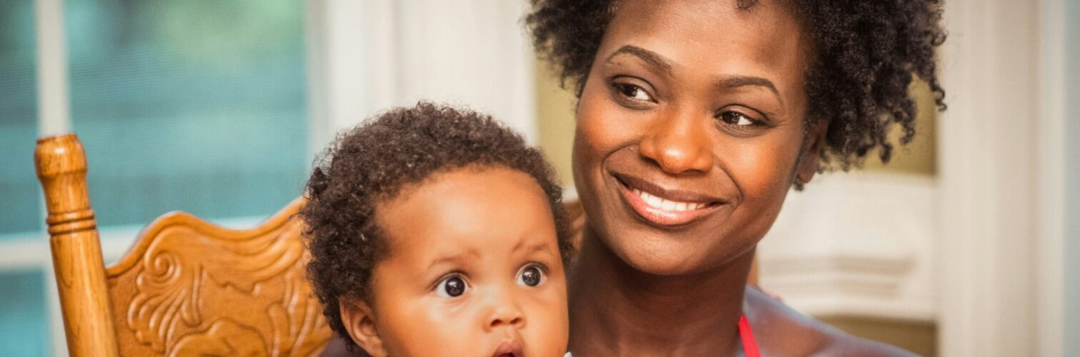 A mother sits smiling with her infant child in a rocking chair