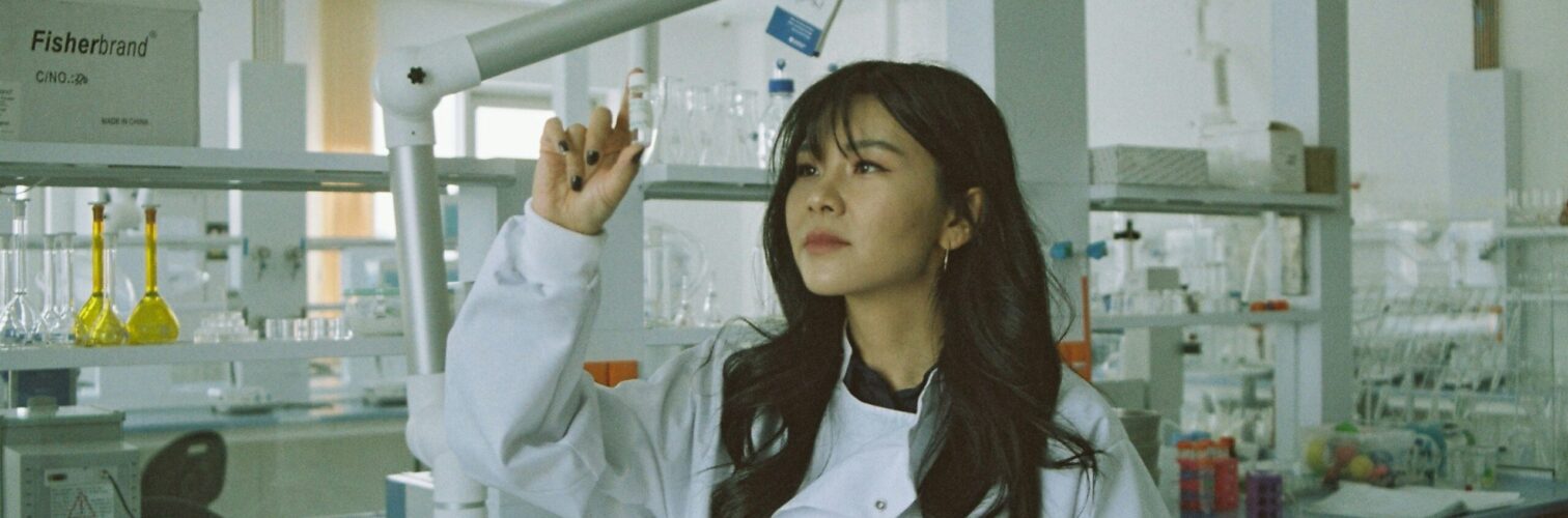 A young female researcher in a lab examines a specimen in a vial.
