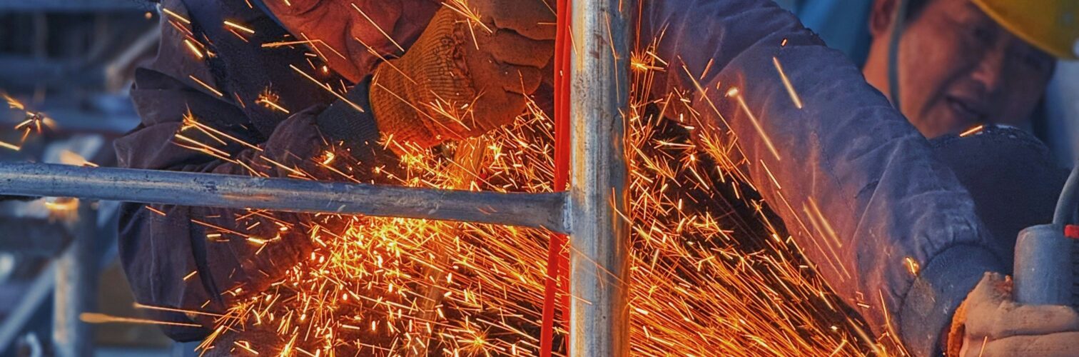 A construction worker in a yellow helmet works while sparks fly from a cutting tool