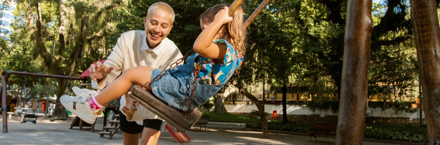 A mother plays with her daughter on a swingset