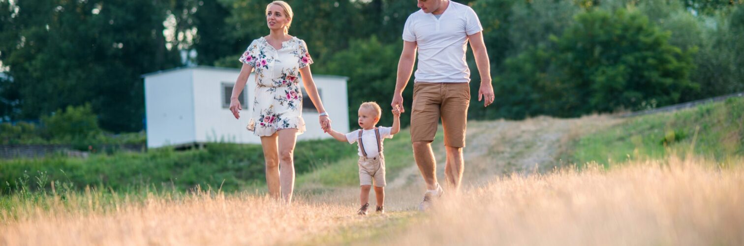 A mother and father walk their toddler down a gravel path through a field