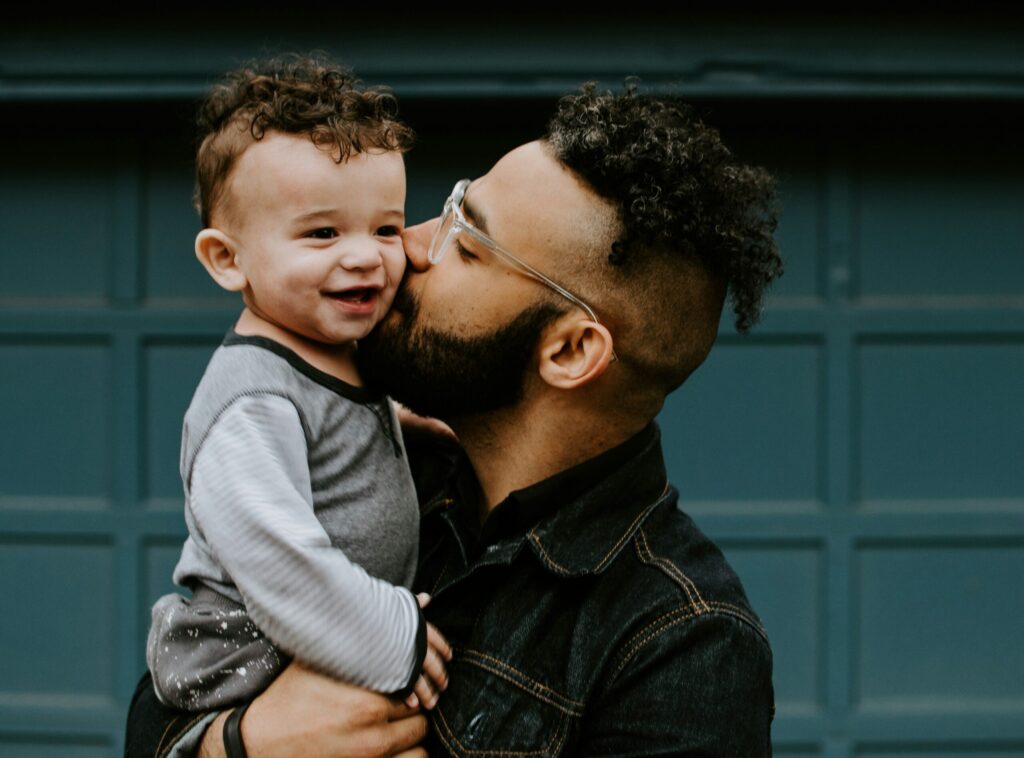 A man holding a smiling boy and kissing his cheek