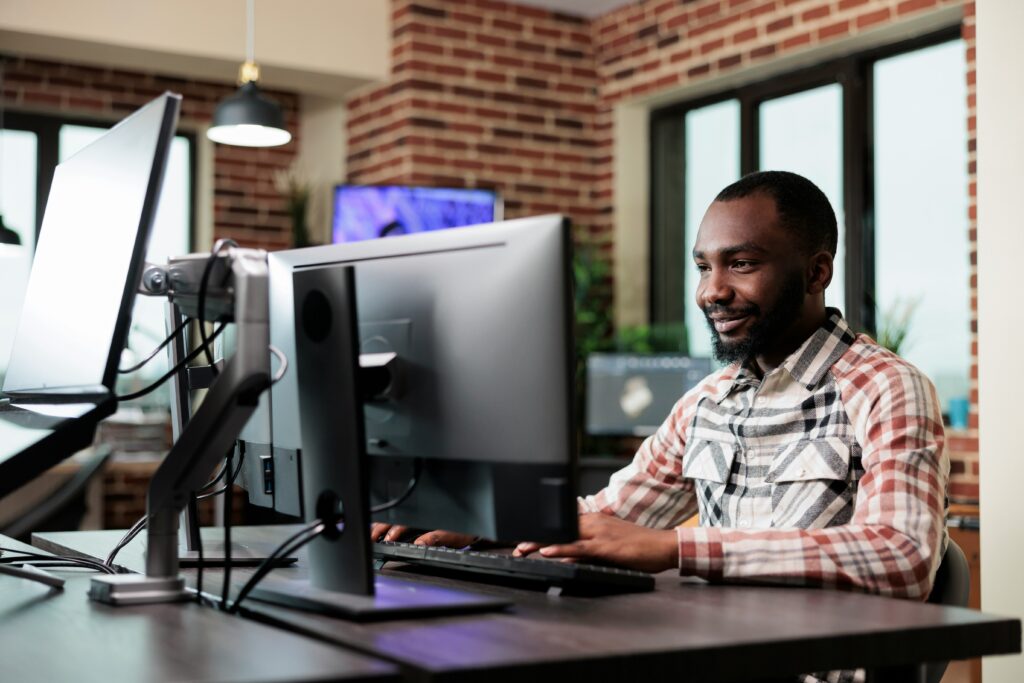 A smiling man sits at a computer terminal in an office setting