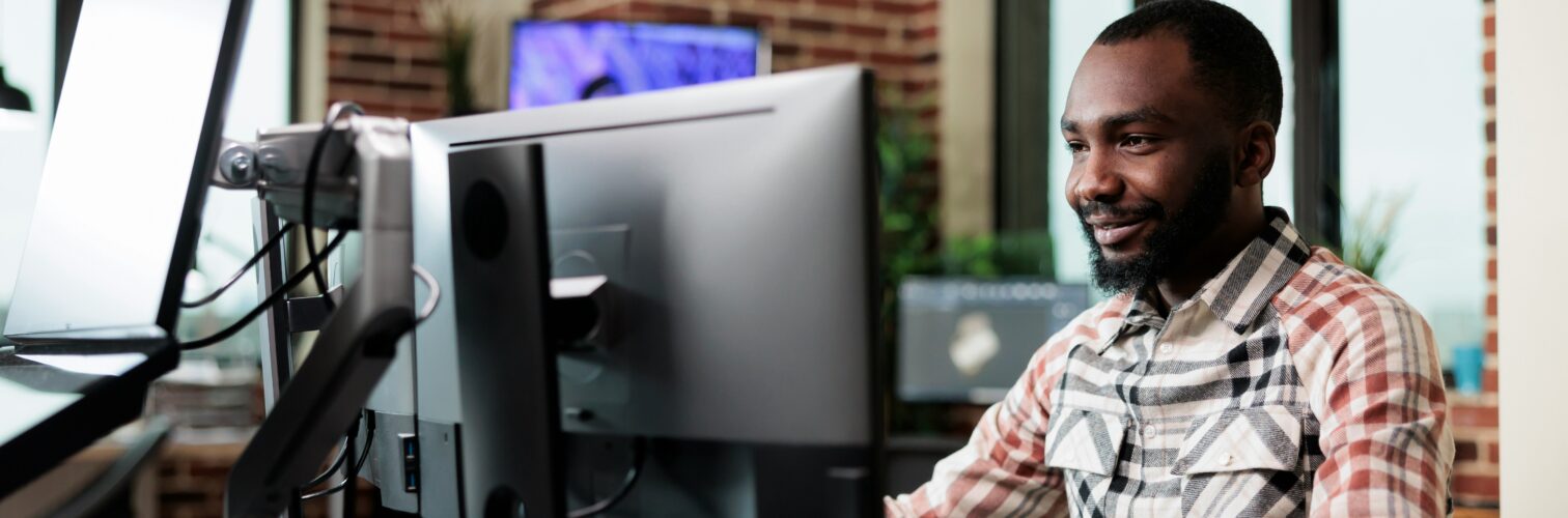A smiling man sits at a computer terminal in an office setting