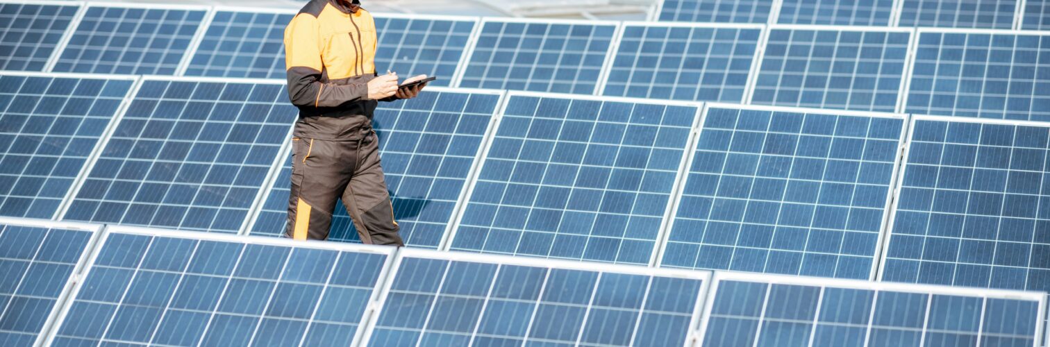 An engineer walks through a field of solar panels and records information