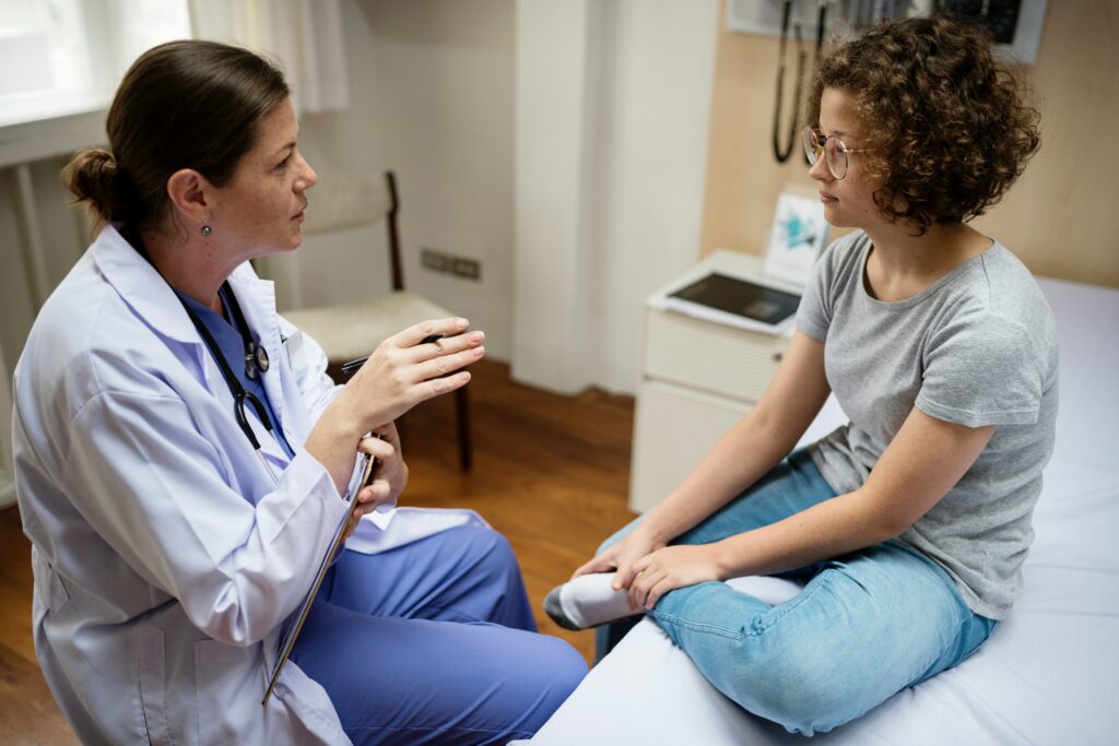 A doctor sits bedside taking with her patient sitting up on an exam table.