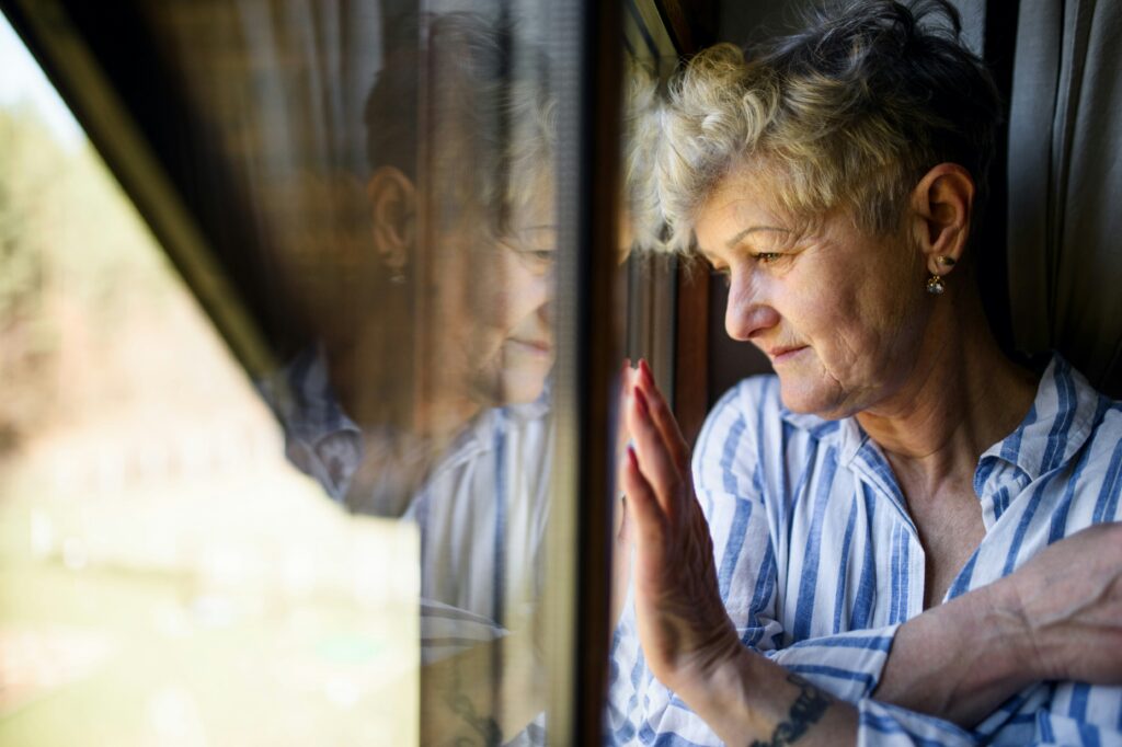 An older woman look forlornly out of her window